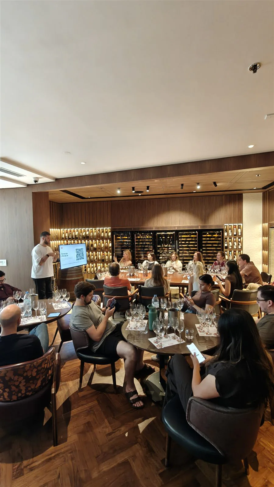Alex Kovalov standing beside a screen with participants seated at tasting tables.