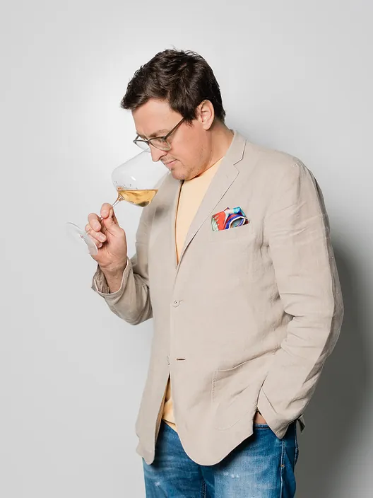 Christiaan Olivier in a linen jacket, nosing a glass of white wine